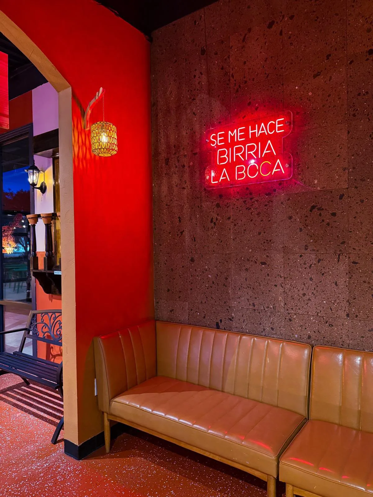 Caramel-colored seating beneath a Se me hace birria la boca neon sign at Jalapeños