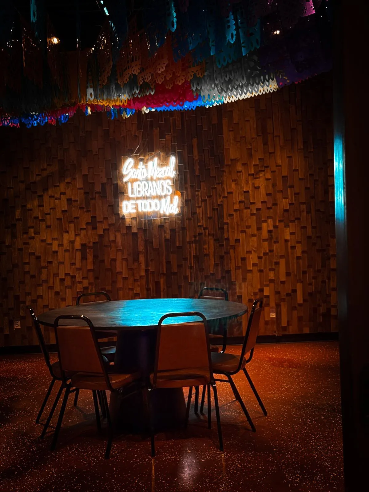 Round dining table under papel picado decorations and a glowing mezcal sign at Jalapeños